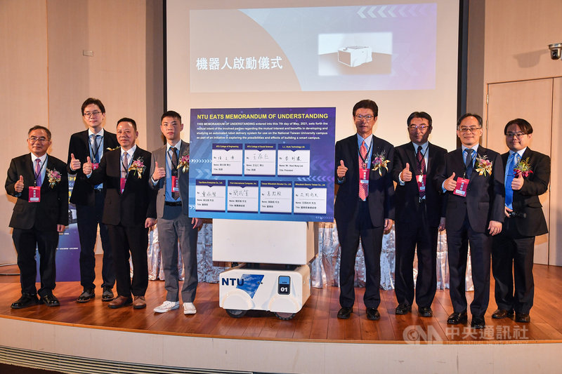 台灣大學7日與國內外多家知名業者共同簽署台大智慧校園自駕送餐計畫NTU EATS合作備忘錄,台大機械系副教授李綱(右)等人與機器人在台前合影。中央社記者鄭清元攝 110年5月7日