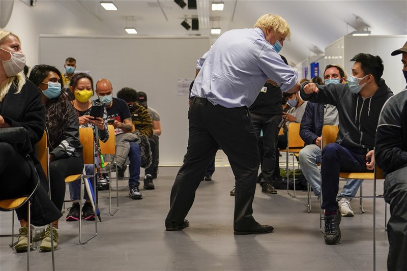英國衛生部政務次長查哈威11日表示,政府有信心19日將會解除英格蘭地區許多防疫限制,但室內密閉空間要配戴口罩的規定預料將會保留。圖為英國首相強生(前中)6月視察疫苗接種站,與等待施打疫苗的民眾相互打氣。(美聯社)