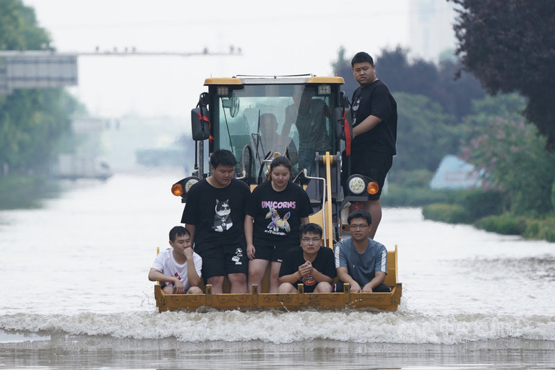河南連日大暴雨。24日在河南新鄉市,民眾乘坐挖掘機通過新中大道一處涉水路段。(中新社提供)中央社 110年7月24日