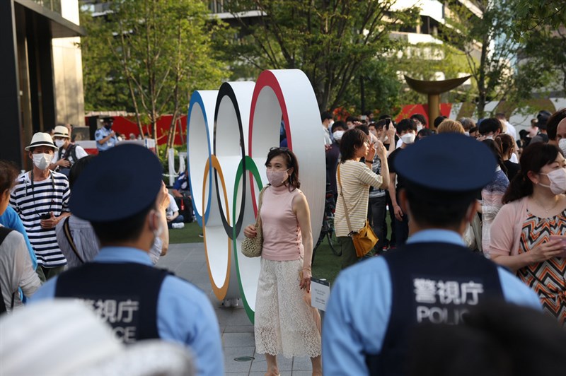 日本東京奧運24日再出傳有選手及警察感染COVID-19,東京都疫情仍未趨緩。圖為民眾跟奧運五環合影留念。(中央社檔案照片)