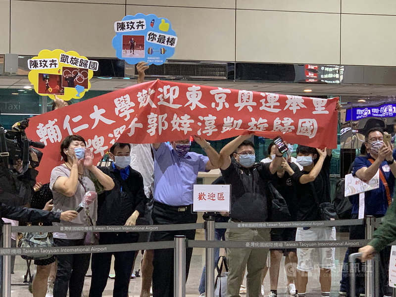 代表台灣出征本屆東京奧運的多名舉重女將郭婞淳、陳玟卉、江念欣等人31日下午搭機返台,機場聚集不少粉絲,高舉紅布條歡迎她們回家。中央社記者葉臻攝 110年7月31日