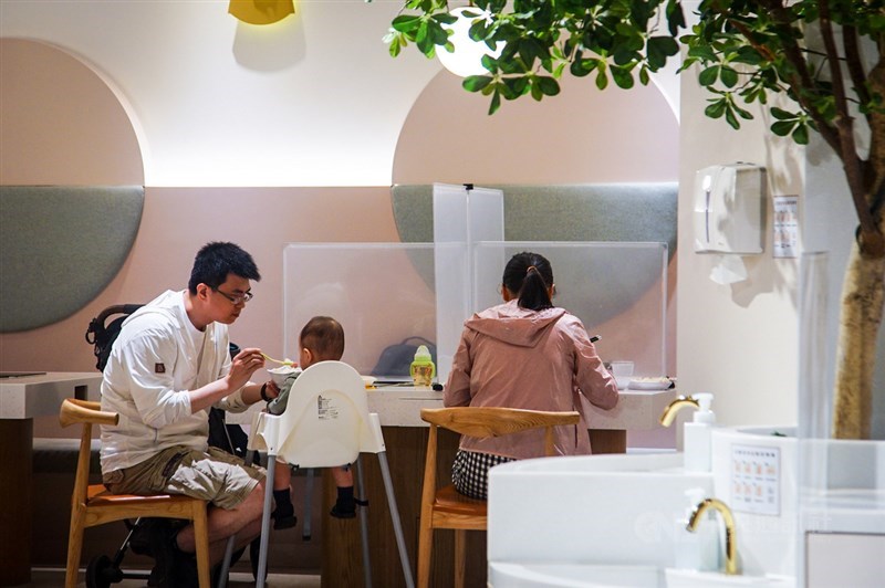 國內疫情降溫,24日起同住親友聚餐不受限使用隔板、梅花座及專人分菜。圖為家長協助幼小孩童用餐。(中央社檔案照片)