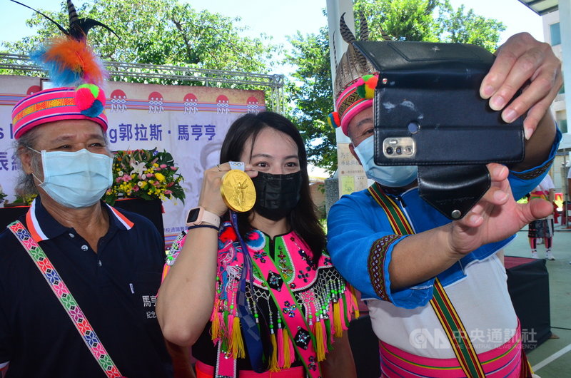 「舉重女神」郭婞淳(中)18日穿著阿美族傳統服飾回到部落,拿出東京奧運金牌與部落分享喜悅,族人爭相拍照合影。中央社記者盧太城台東攝 110年9月18日