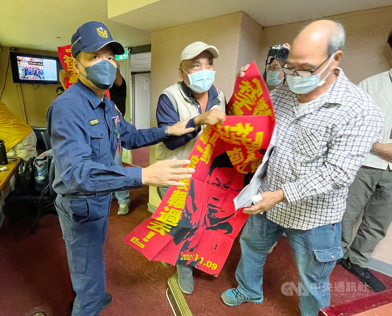 台北市議會19日持續進行市政總質詢,市長柯文哲列席備詢,多名社子島自救會成員手持紅色海報,突然闖進議會記者旁聽席表達抗議,警衛隨即上前阻止。中央社記者郭日曉攝 110年11月19日