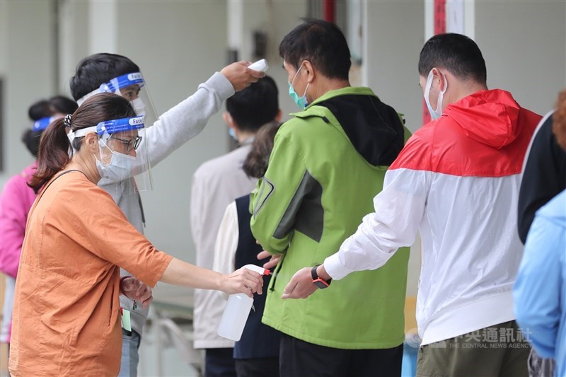 WHO會員國下週將召開特別衛生大會會議,討論是否制訂一項防範和應對疫情大流行條約。圖為民眾依序進入室內前量測體溫並以酒精消毒雙手。(中央社檔案照片)
