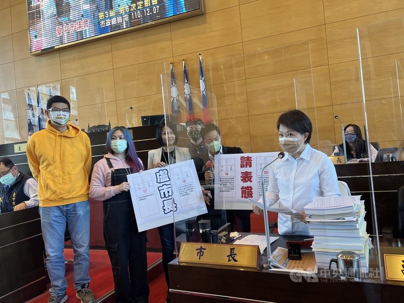 台中市議會第3屆第6次定期會7日起展開市政總質詢,民進黨籍台中市議員蔡耀頡(前右2)等人拿著看板到官員備詢席,要求市長盧秀燕(前右)就4項公投議題表態。中央社記者郝雪卿攝 110年12月7日