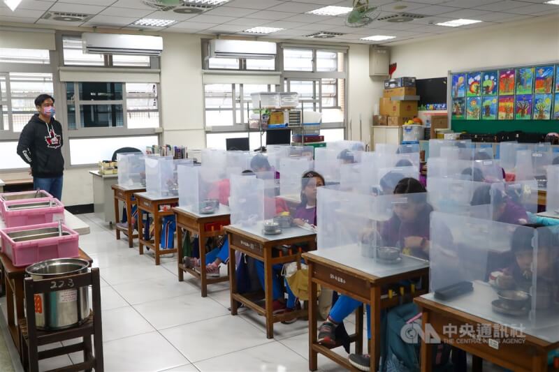 台北市政府19日宣布寒假課輔、社團活動暫停到2月底。教育部表示,尊重各縣市政府考量。圖為17日國小學生用餐時使用隔板,做好防疫措施。(中央社檔案照片)