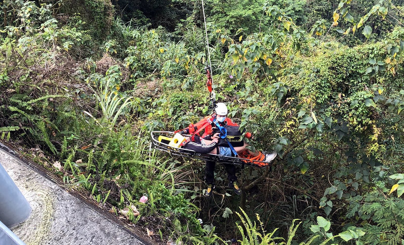 嘉義縣台3線中埔路段13日發生一部機車自摔，乘客鄭姓男子摔落10公尺深邊坡，救援人員以器材車吊臂吊掛籃式擔架搶救，鄭男左腳骨折，全身多處擦挫傷。（嘉義縣消防局提供）中央社記者黃國芳傳真  111年2月13日