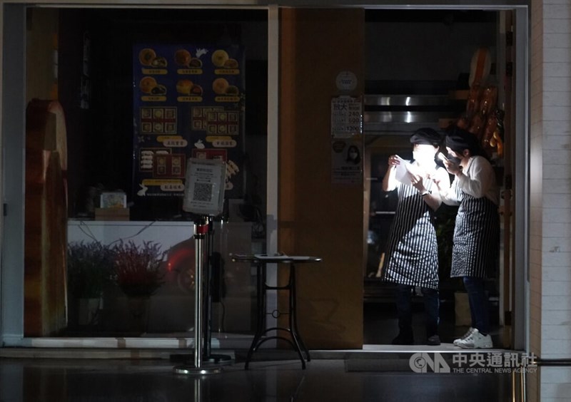 高雄地區入夜後仍有多處遲未復電。圖為一家糕餅業者員工晚間藉由手機燈光互相討論。中央社記者董俊志攝 111年3月3日
