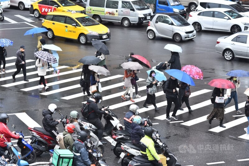 中央氣象局27日表示,未來一週2波東北季風影響。圖為台北市區民眾撐雨傘過馬路。(中央社檔案照片)
