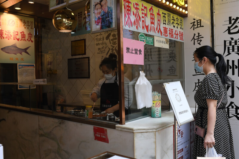 圖為12日廣州市越秀區一間餐飲店貼著禁止內用(堂食)告示,店員為外帶顧客打包餐點。(中新社)