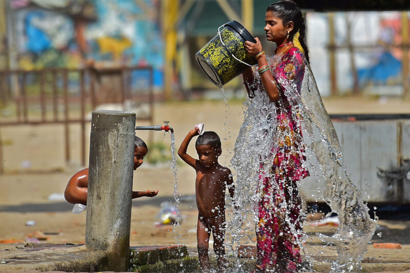 印度、巴基斯坦3月和4月深陷熱浪煉獄。圖為4月28日印度一名婦女和孩子用路邊的水龍頭沖洗身體。（法新社）