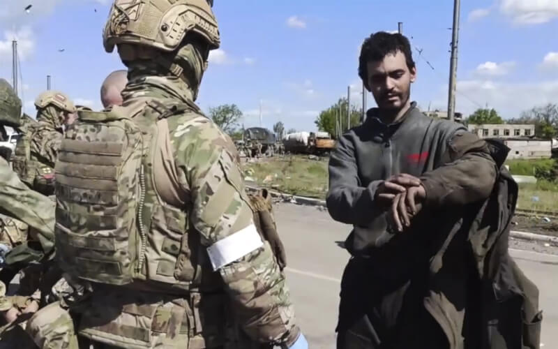 俄國國防部日前發布影片內容顯示烏克蘭投降士兵（右）步出亞速鋼鐵廠，有些人明顯受了傷，俄軍（前左）進行拍身搜查並檢查他們身上的包包。（美聯社）