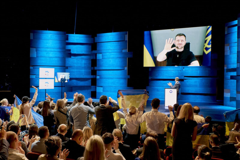 圖為烏克蘭總統澤倫斯基9日在哥本哈根民主峰會視訊演說，台下聽眾起身鼓掌，還有人高舉烏克蘭國旗致意。（圖取自twitter.com/AndersFoghR）
