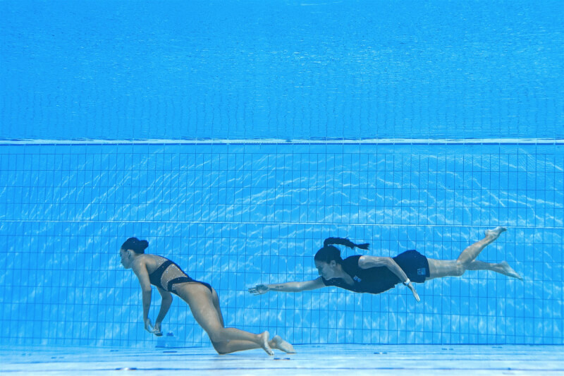 美國水上芭蕾選手阿爾瓦雷茲（左）22日出賽時，完成自選動作後突然昏厥沉入池底，教練連忙跳下水將她救出。（法新社）
