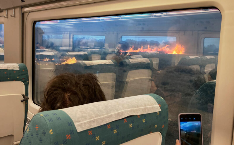 西班牙國營鐵路公司說，由於火勢靠近鐵軌，西北部兩個地區之間的列車18日早晨停駛。圖為列車上的乘客拍下窗外野火火勢。（美聯社）