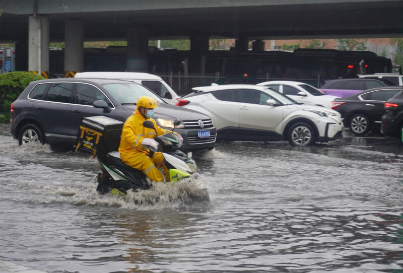 去年造成約400人喪生的河南水災近日滿週年，當地再遇暴雨，省會鄭州市多地淹水。圖為22日鄭州外送員在雨中行駛。（中新社）