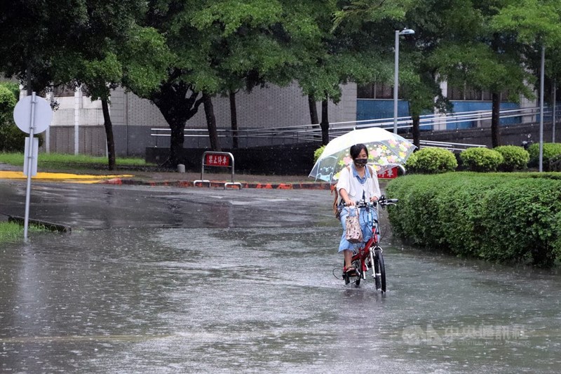 中央氣象局29日表示，接下來的天氣受低壓帶逐漸靠近影響，將帶來水氣及降雨，但高溫仍在攝氏32度以上。圖為4日新莊民眾撐著傘騎腳踏車經過積水的道路。（中央社檔案照片）
