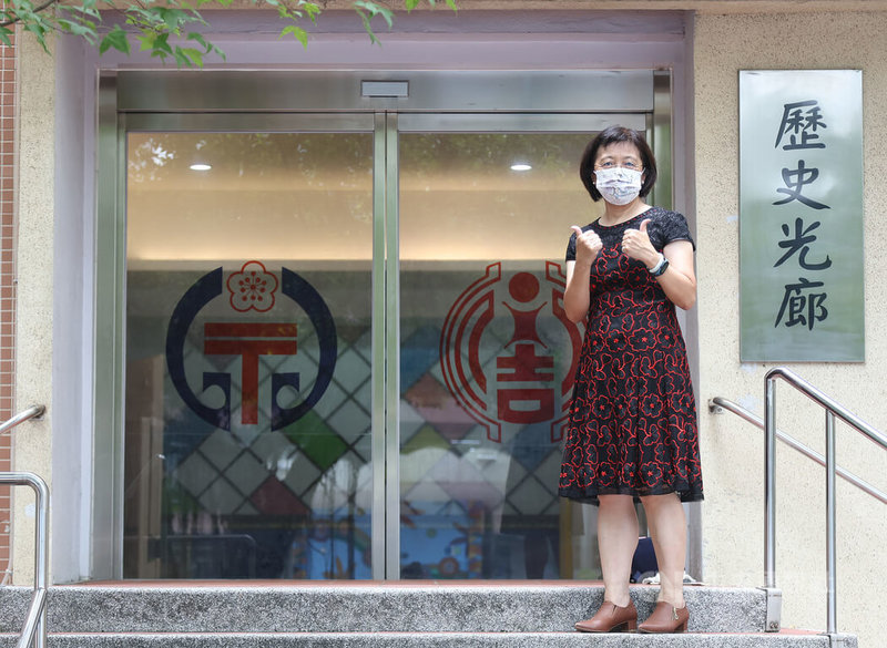 僅一牆之隔的台北市信義區永春國小與永吉國小配合市府推動市有建物及用地整合運用教育導向的都市發展(EOD)計畫,111學年度正式合併成立為雙永國民小學。前永春國小校長黃淑茹完成階段性任務,1日出席揭牌儀式,在歷史光廊前與兩校校徽合影。中央社記者張新偉攝 111年8月1日