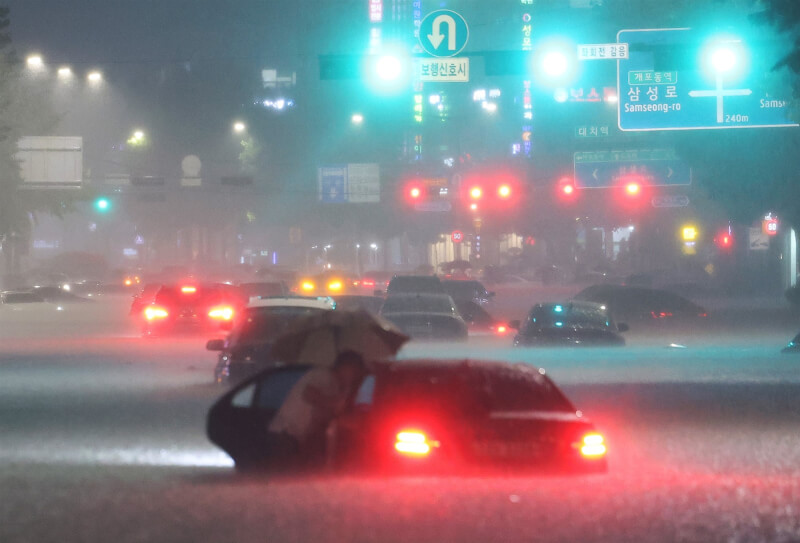 韓國中部地區8日起暴雨不斷，首都圈等地區災情頻傳，至少7死、6人失蹤。圖為8日晚間首爾江南區有輛轎車遭水淹過輪胎，駕駛開門離開現場。（韓聯社）