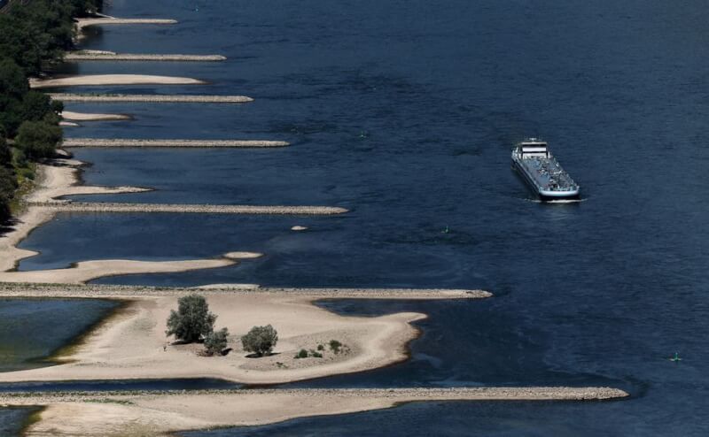 圖為9日一艘運輸船駛過德國賓根萊茵河部分乾涸的河床。（路透社）