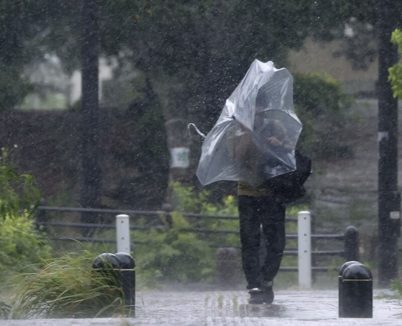 圖為日本沖繩縣那霸市民眾3日在風雨中勉強撐傘行進。（共同社）