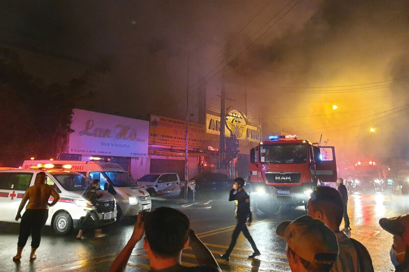 越南平陽省順安市「安富卡拉OK」6日晚間火警釀33死11傷，其中3人重傷。圖為消防及救護人員抵達事故現場，建築物冒出濃煙。（法新社）