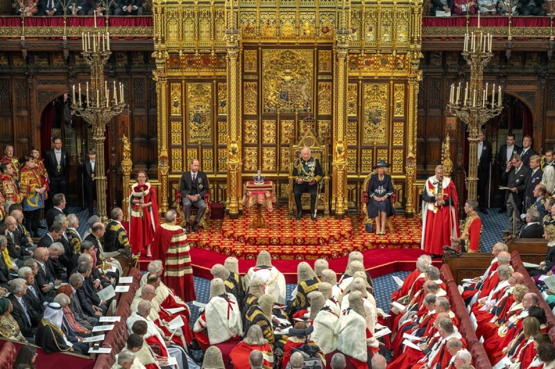 圖為英國國會5月10日新會期開議大典，查爾斯（後方面向鏡頭坐立者右2）代替女王伊麗莎白二世發表御座致辭。女王的御座由置放在桌上的王冠取代。（英國國會上議院提供）中央社記者陳韻聿倫敦傳真 111年5月10日
