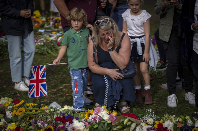 圖為10日倫敦白金漢宮附近的綠園，一名婦女在紀念英國女王的鮮花旁哭泣。（美聯社）