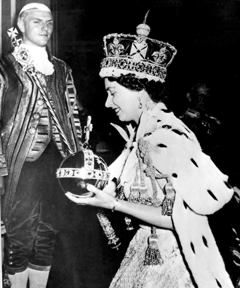 圖為英國女王伊麗莎白二世1953年登基時，戴著鑲有寶石的皇冠，並拿著寶珠和權杖。（美聯社）