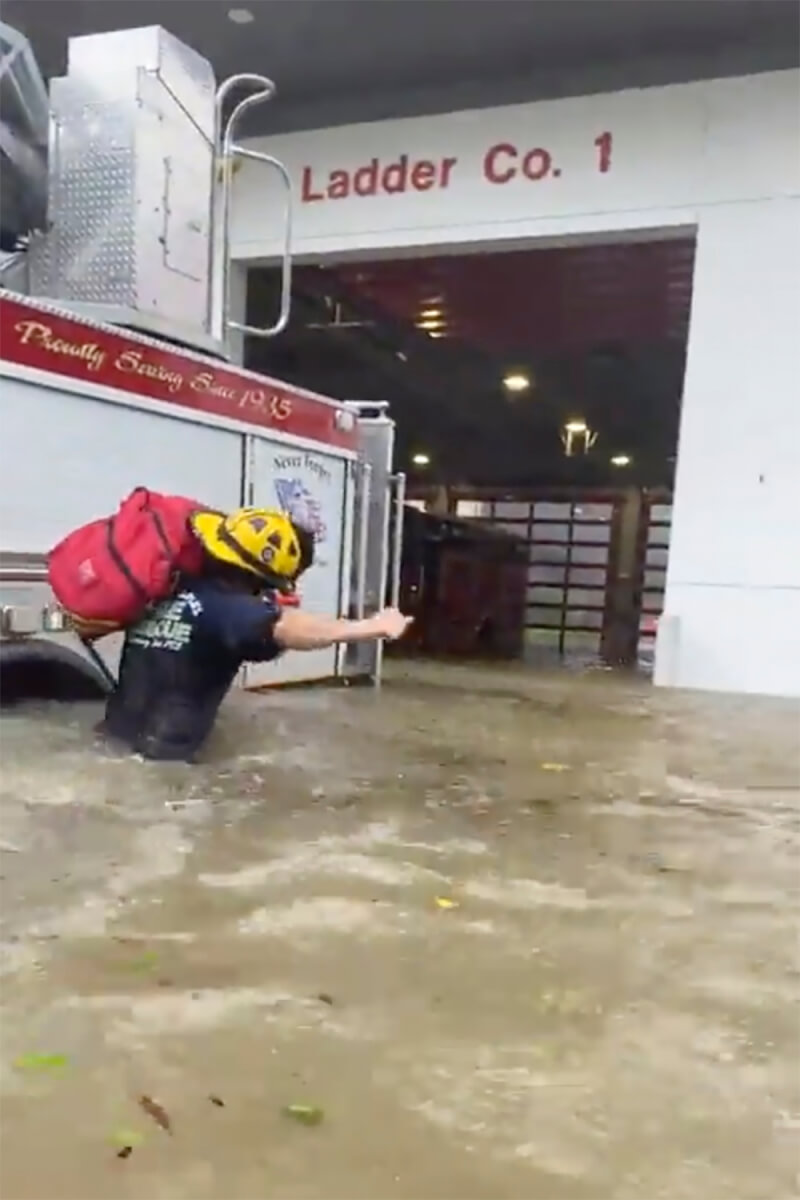 佛州一處消防單位28日受颶風伊恩影響湧進大水，水深一度及腰，消防人員只能在風雨中涉水搬運救援工具。（佛州那不勒斯消防隊 via 美聯社）