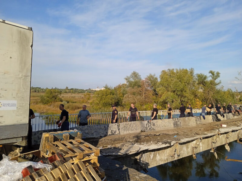 烏克蘭消防人員和民間志工29日經由橋上完好無損的人行通道，運送第一批人道援助糧食進庫皮揚斯克。（圖取自facebook.com/MNS.GOV.UA）