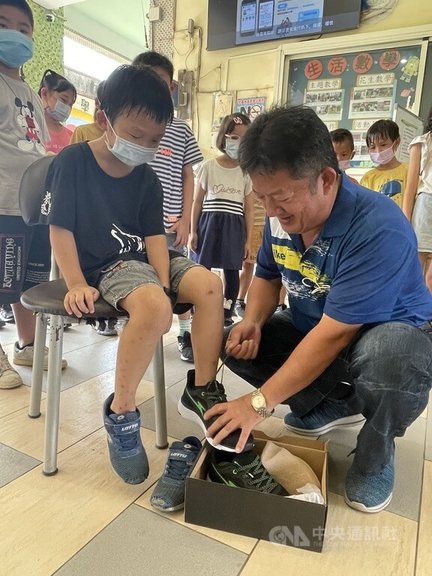 雲林縣元長鄉企業家李坤煌（前右）連續5年送元長鄉10所國中小學弱勢家庭學生新球鞋，他4日到母校山內國小送新鞋時，一眼發現二年級男童腳上穿的是去年送的鞋子，他並協助男童試穿新鞋。中央社記者姜宜菁攝  111年10月4日