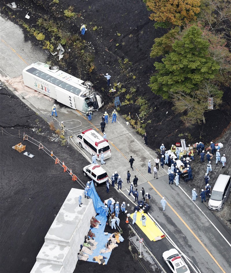 一輛大型觀光巴士13日行經靜岡縣一處縣道時翻車，救援人員抵達事發現場協助傷患。（共同社）