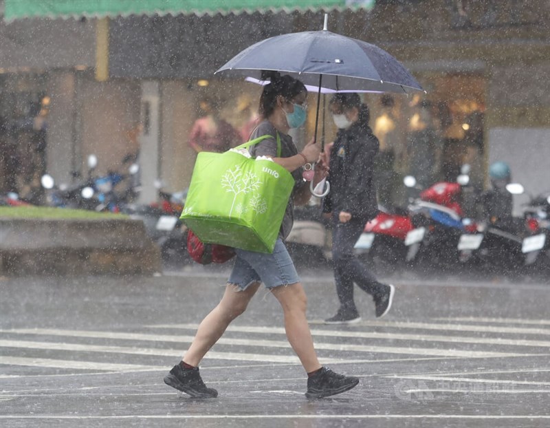 氣象局表示，15日受熱帶性低氣壓或颱風外圍環流接近影響，北部及東半部有局部大雨或豪雨發生的機率。圖為走在台北市信義區街頭的民眾撐傘遮擋雨勢。（中央社檔案照片）