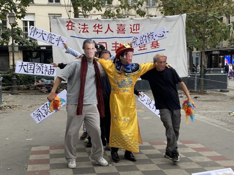 旅法青年團體「自由廣場」16日在巴黎龐畢度中心旁的廣場舉行抗議活動，架起「在法華人喜迎習主席登基」的看板，並演出諷刺行動劇。習近平身著龍袍左擁俄國總統蒲亭，右抱法國總統馬克宏。中央社記者曾婷瑄巴黎攝 111年10月17日