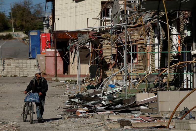 圖為18日一名男子行經烏克蘭東北部市鎮庫皮揚斯克被俄軍摧毀的購物街。（路透社）