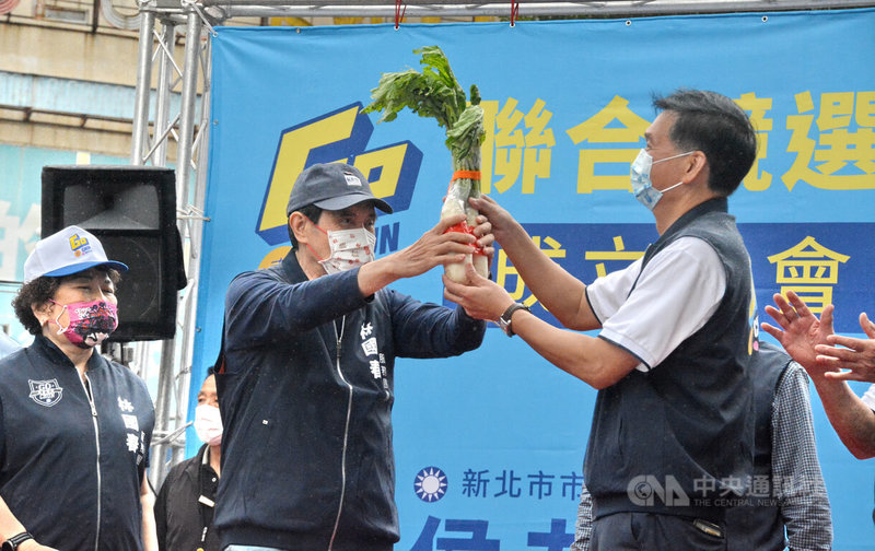 前總統馬英九（中）23日前往新北市板橋區參加國民黨籍新北市議員林國春競選總部成立大會，為林國春（右）站台助選，並致贈象徵好彩頭的菜頭。中央社記者黃旭昇新北攝  111年10月23日