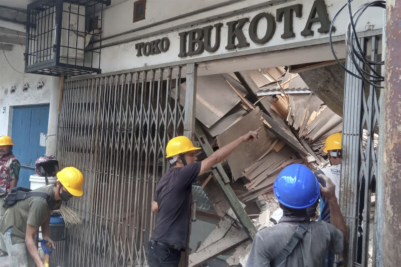 21日震後，工人們緊急檢查因地震毀損的商店。（美聯社）