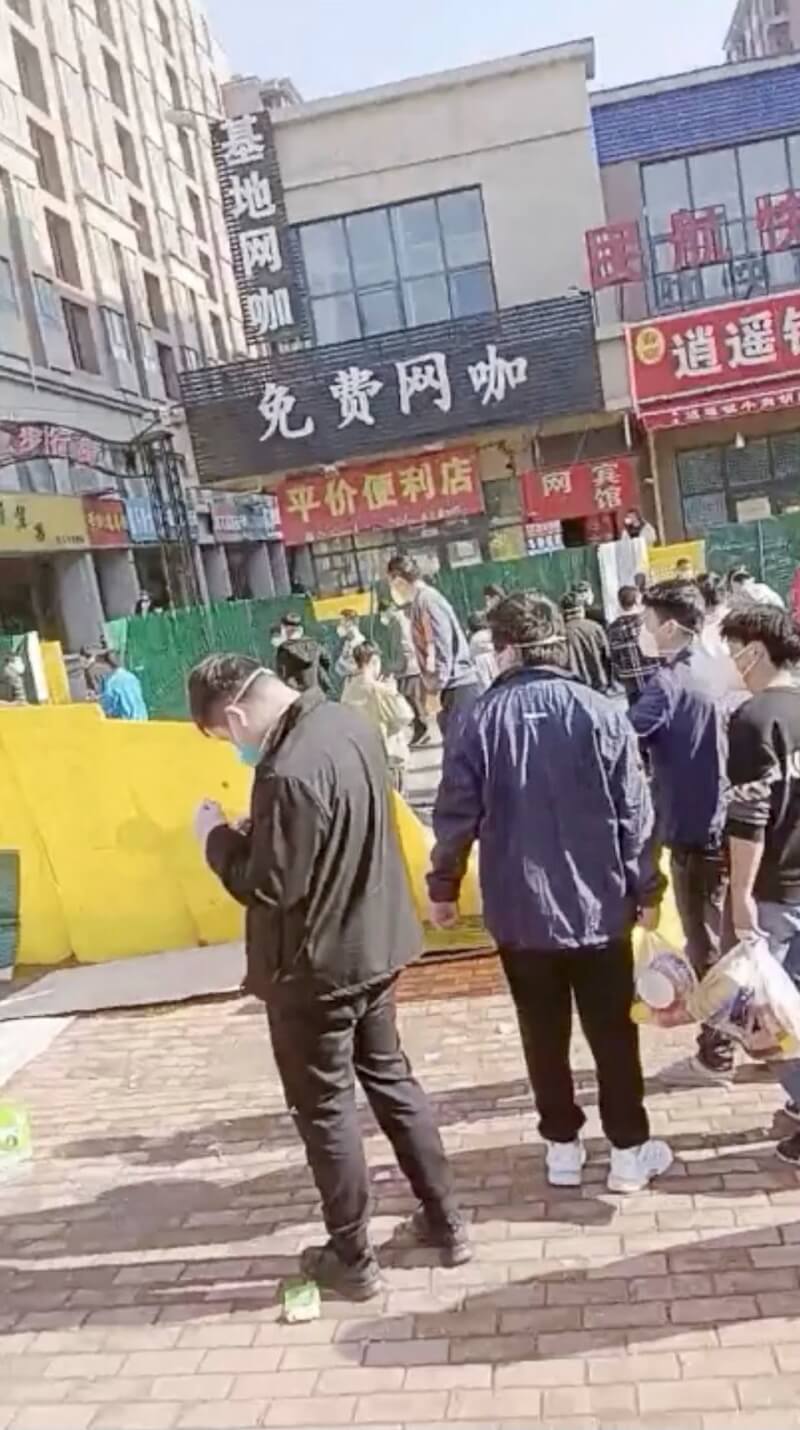 路透社截取23日社群上的影音畫面顯示，在中國鄭州富士康廠區爆發抗議活動後，一群人穿過倒塌的圍欄。（翻攝畫面／路透社）