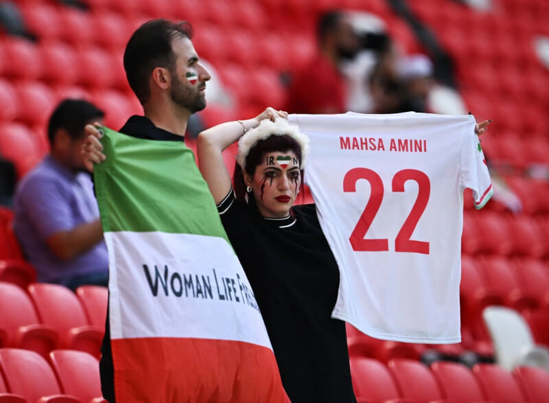 圖為25日伊朗粉絲在伊朗對威爾斯賽前舉著支持女權的旗幟及紀念庫德族女子艾米尼的衣服。（路透社）