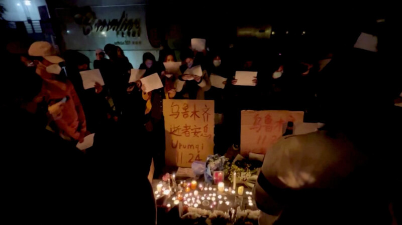 上海民眾26日在為烏魯木齊火災罹難者舉行的守夜活動中手舉標語並點亮蠟燭。（翻攝畫面／路透社）