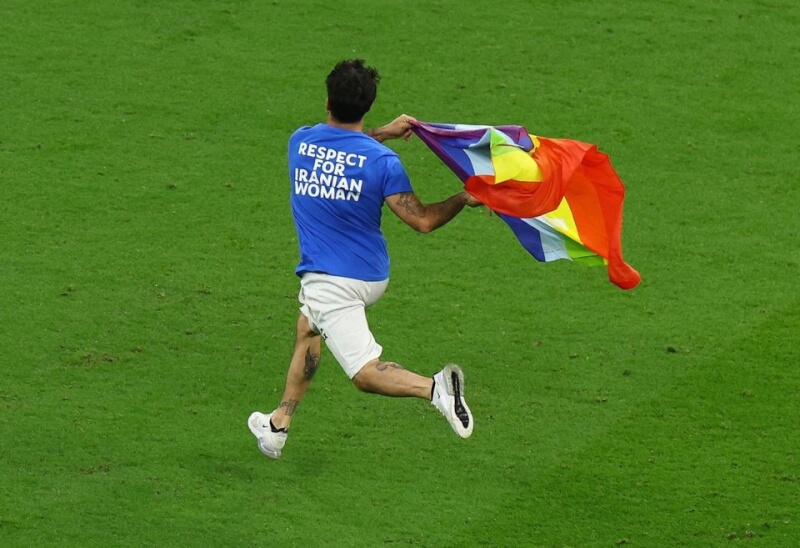 世界盃足球賽28日比賽期間發生抗議插曲，一名男子手持彩虹旗闖入場中，身上穿的T恤背面寫著「尊重伊朗女性」。（路透社）