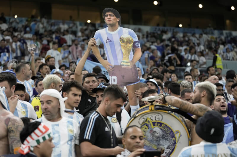 阿根廷將在2022卡達世足賽與法國爭冠，阿根廷傳奇球星馬拉度納的兒子席納格拉表示，「我父親會為他們如此為國爭光而感到驕傲。」圖為阿根廷球迷在看台舉起馬拉度納人形看板。（美聯社）