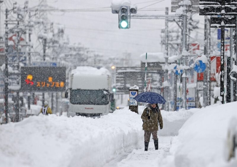 日本新潟縣降下破紀錄大雪，已造成2死6傷。圖為20日在新瀉積雪街道行走的民眾。（共同社）