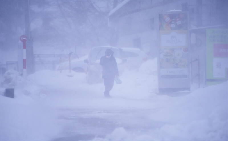 日本山形縣民眾23日在暴風雪中行走。（共同社）