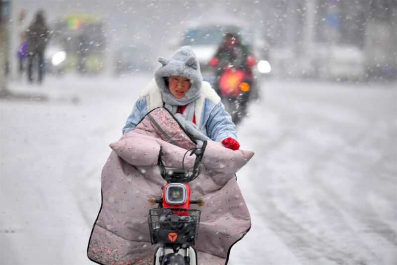 圖為24日安徽省毫州市區民眾穿著禦寒衣物冒雪騎車。（中新社）