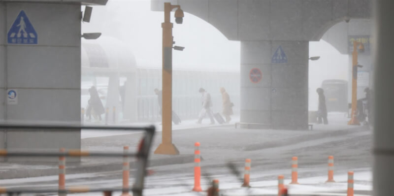 超強寒流襲韓，位於最南部的濟州道因暴雪、強風停飛所有航班。圖為24日上午民眾冒著大雪走在濟州國際機場前的道路。（韓聯社）