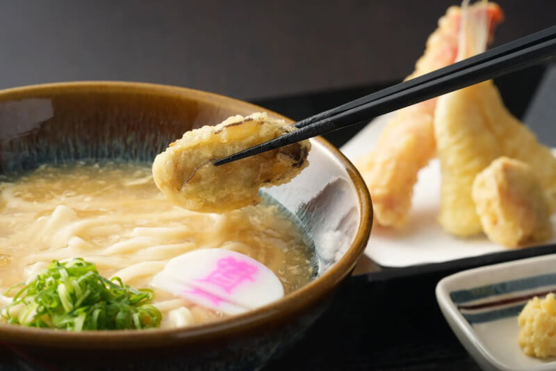 日本連鎖烏龍麵店桌上免費食材被人惡搞， 一名男性顧客用公用湯匙大口吃放在餐桌上、供所有顧客取用的炸物炸渣。（圖取自twitter.com/sukesan1976）