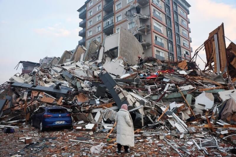 土耳其當地時間6日凌晨發生規模7.8強震，7日土耳其南部哈泰省一名婦人站在瓦礫堆前觀看救援過程。（路透社）